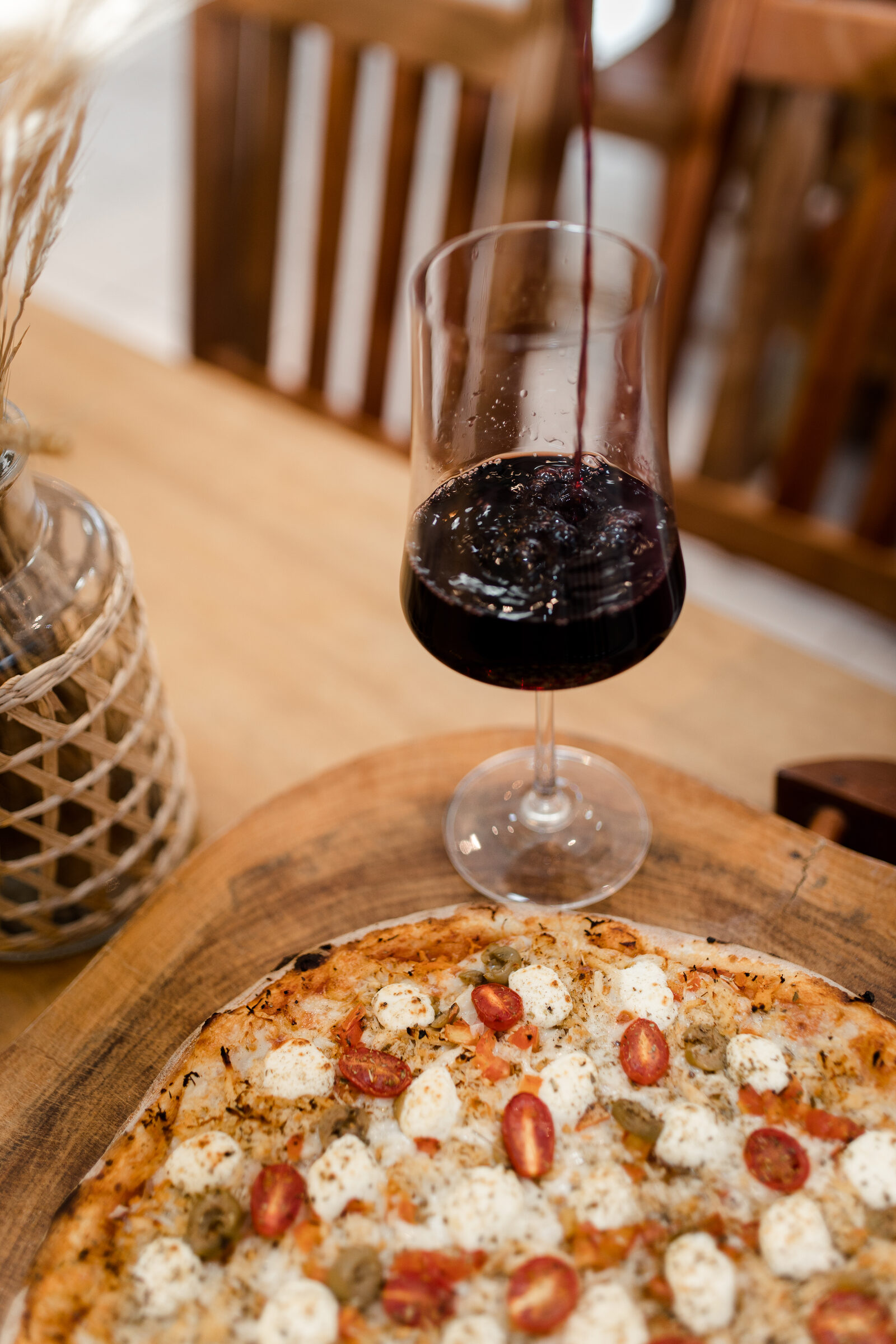 Vinho sendo servido na mesa da Cia Casero, com a pizza na tábua